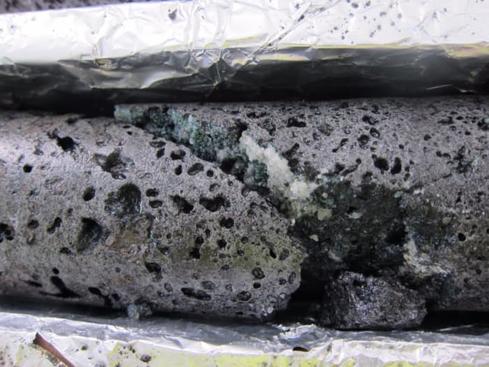 A fractured basalt rock reveals the white calcium carbonate crystals that formed after the addition of CO2 to the underground well